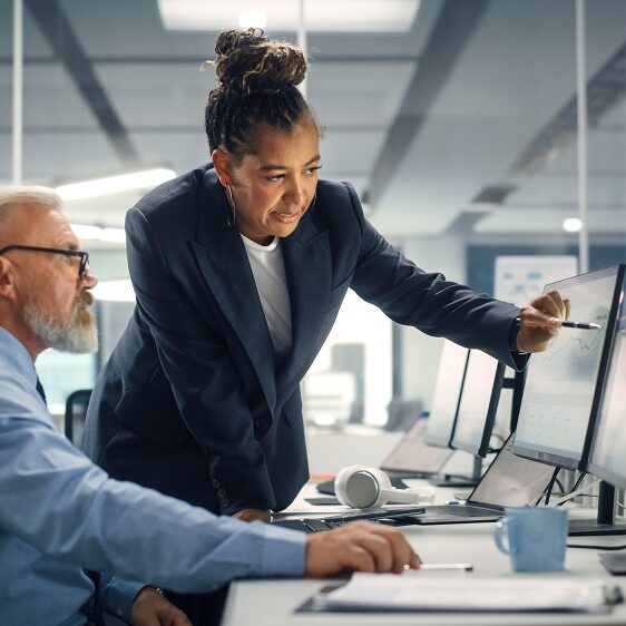 Senior Manager Talking to Experienced Confident Businessman while Using Computer in Modern Office. Colleagues Discuss Commercial, Financial and Marketing Projects. Specialists Work in Diverse Team.